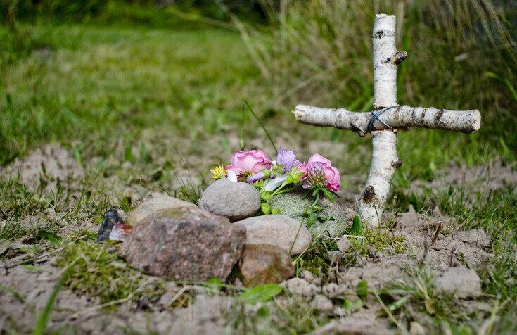 wooden cross next to pile of rocks and flowers